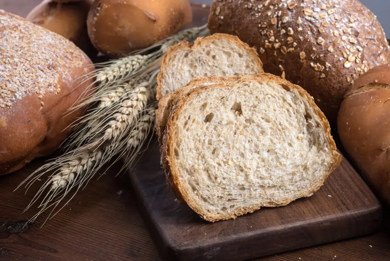 Różnorodne pieczywo, w tym bochenki z ziarnami i kromki chleba pełnoziarnistego. Idealne, gdy zastanawiasz się, jakie pieczywo przy odchudzaniu wybrać.