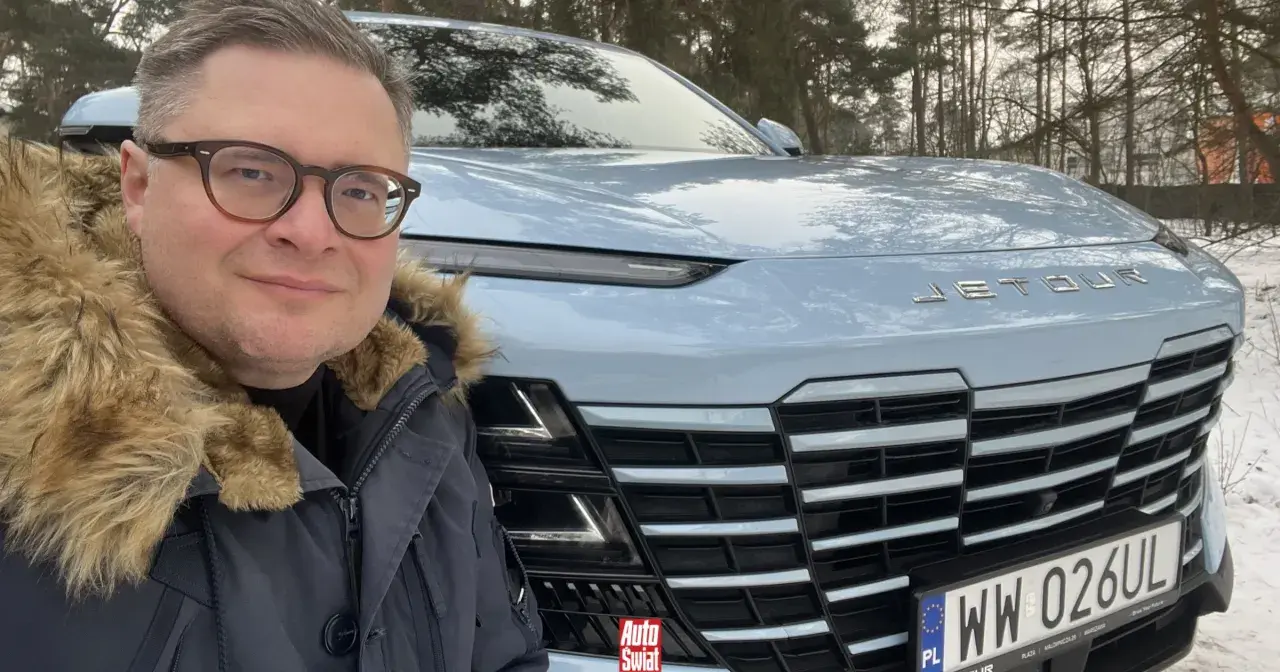 Mężczyzna w okularach i futrzanej kurtce pozuje do selfie przed jasnoniebieskim Jetour Dashing na tle zimowego lasu.
