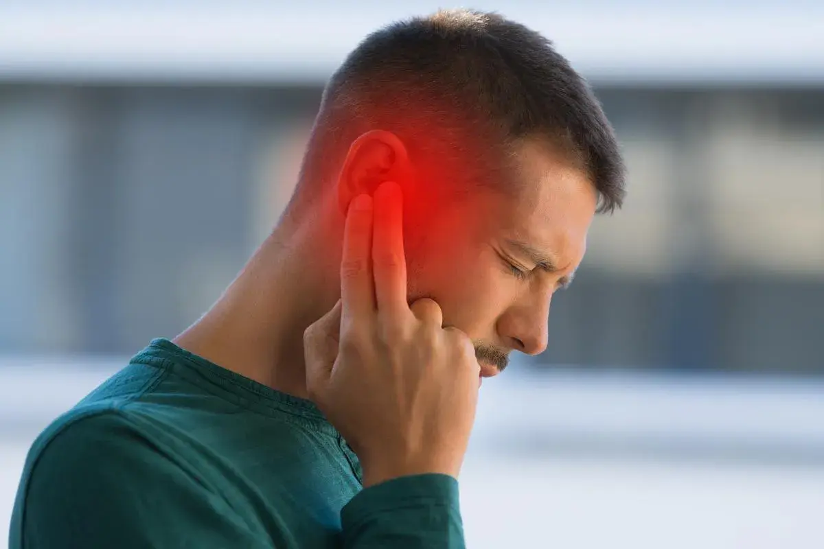 Hombre con dolor de oído, señalando la zona afectada con un halo rojo. Podrían ser sabañones en las orejas.