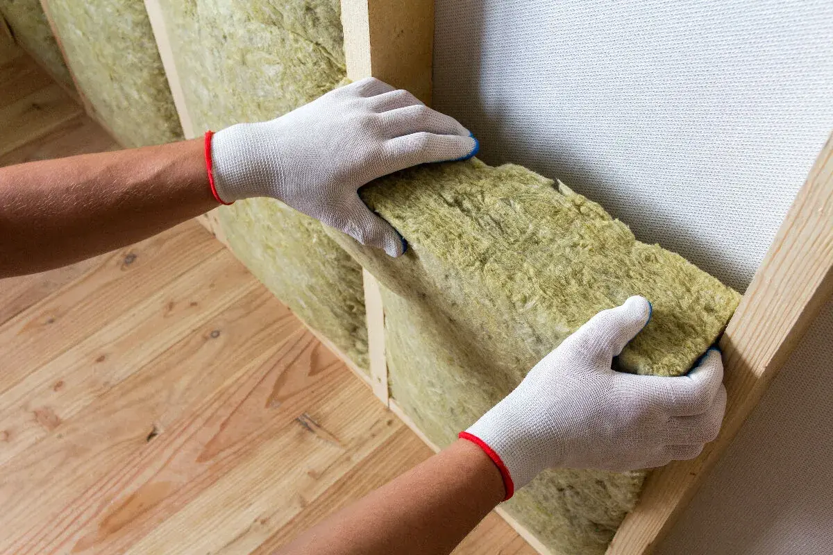Pose d'isolant dans une structure de mur en bois. L'isolation aide à prévenir l'humidité du mur et améliore le confort thermique.