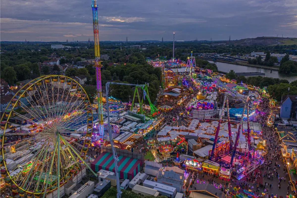 Buntes Lichtermeer auf Volksfesten im Herbst: Riesenrad, Hochbahn und Fahrgeschäfte beleuchten die Nacht.