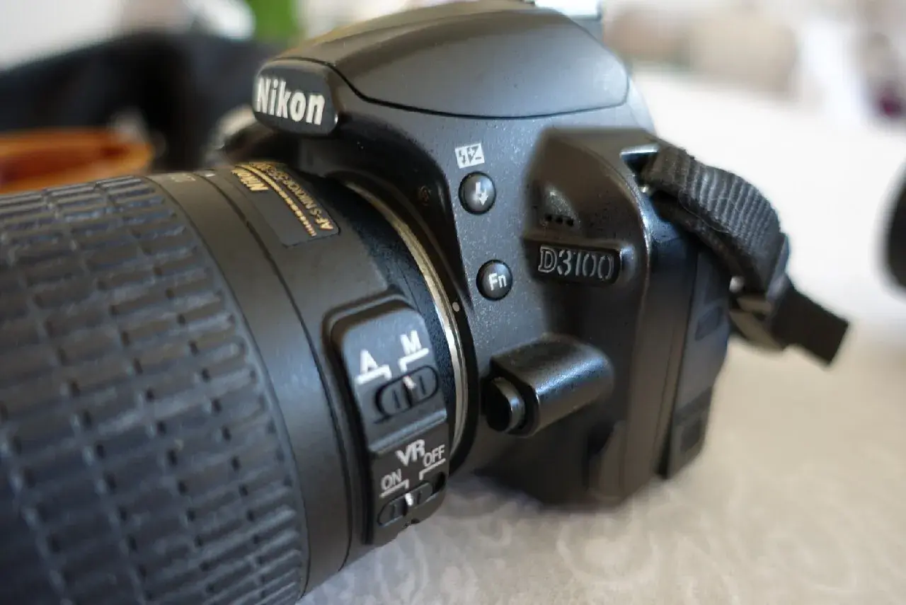Zbliżenie na aparat Nikon D3100. Widoczny obiektyw z pierścieniem ostrości i przełącznikami AF/M oraz VR ON/OFF. D3100 to model, którego nikon d3100 dane techniczne warto poznać.