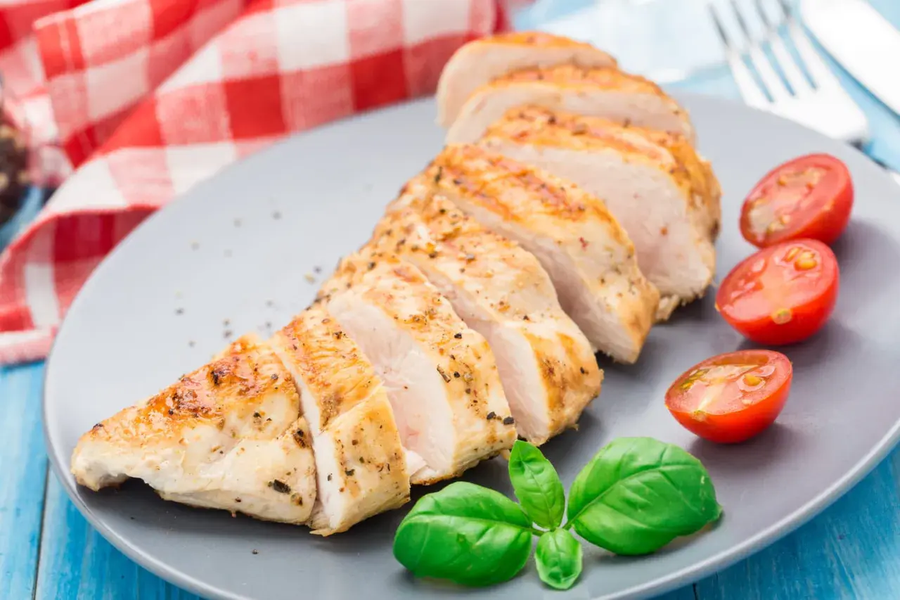 Tranches de blanc de poulet grillé, assaisonné de poivre et d'herbes, servi avec des tomates cerises et du basilic frais.