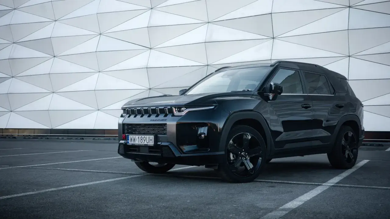 Czarny SsangYong Torres z czarnymi felgami stoi na parkingu przed nowoczesnym budynkiem o geometrycznej fasadzie.