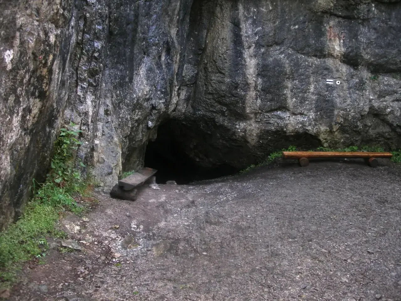 Wejście do jaskini w skale, obok ławka i kamienna ława. Tajemnicza dziura w górach, może w okolicach Zakopanego.