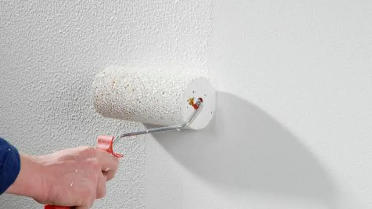 Eine Hand rollt mit einem Farbroller eine strukturierte Wand. Der Rollputz innen wird aufgetragen und verleiht der Oberfläche eine interessante Textur.
