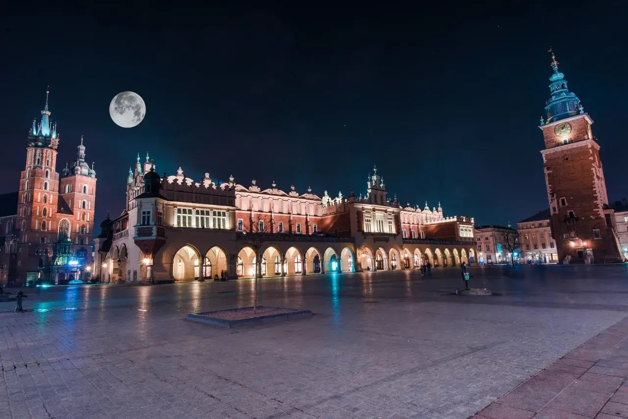 Kraków nocą. Sukiennice i Kościół Mariacki pod księżycem. Wieża Ratuszowa góruje nad Rynkiem.