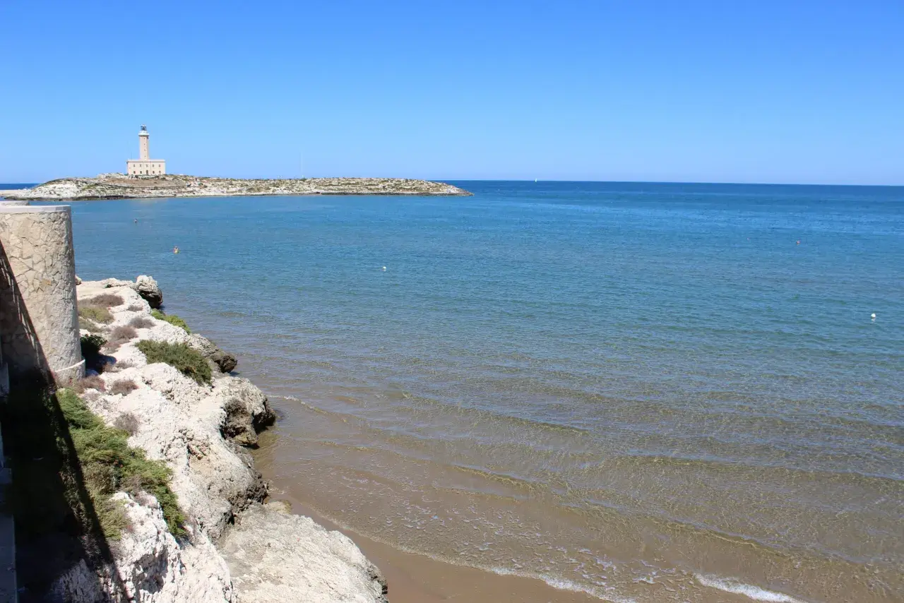 Faro di Vieste, Stella Maris, su un'isola rocciosa con mare azzurro e spiaggia sabbiosa.