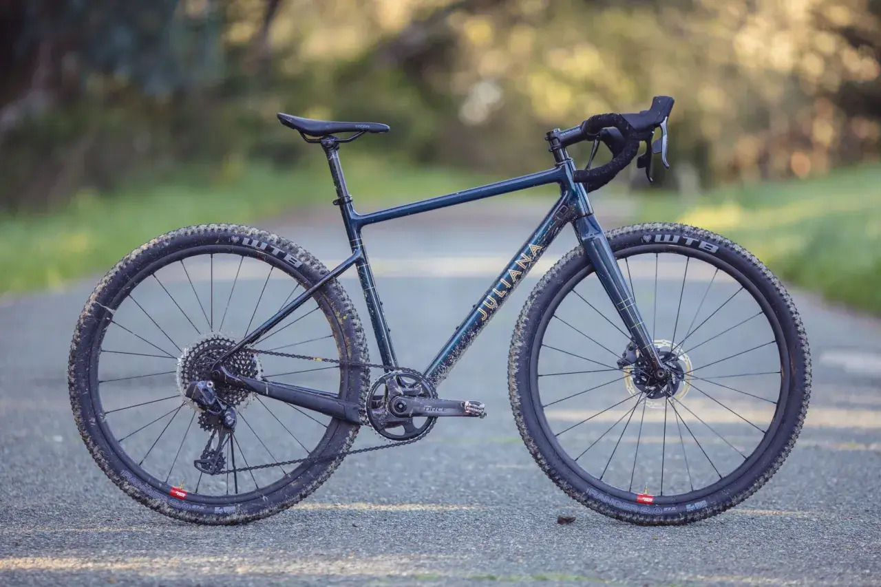 A dark blue Juliana gravel bike with gold lettering sits on a paved path, ready for adventure.