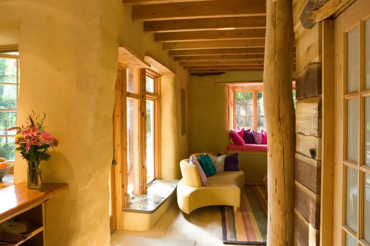 Interno accogliente con pareti in intonaco terra cruda, mobili in legno grezzo e un divano giallo con cuscini colorati.