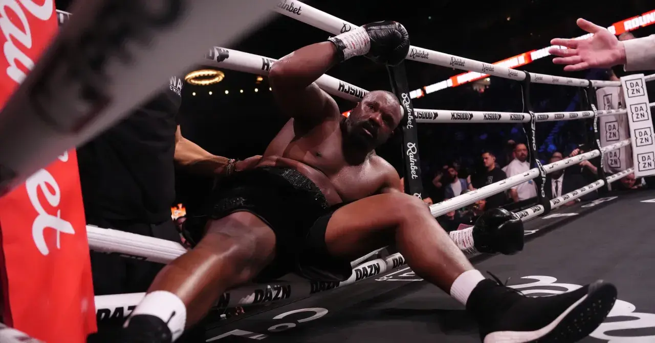 Derrick Chisora klęczy na macie, wyczerpany po walce. W tle widać publiczność i ring bokserski.