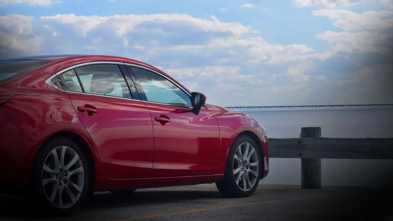 Czerwona Mazda 6 2.0 benzyna zaparkowana nad wodą, z mostem w tle.
