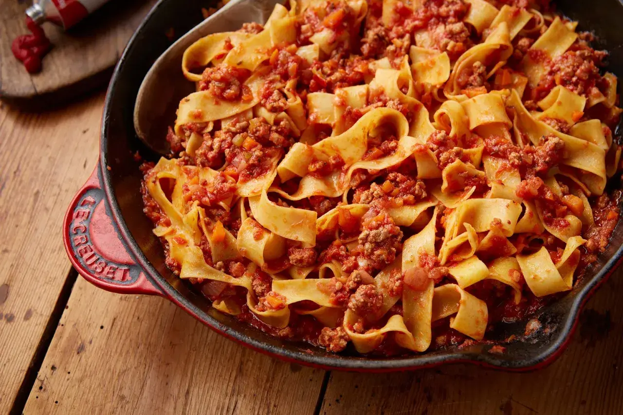 En stor portion krämig pasta bolognese i en röd gjutjärnspanna.