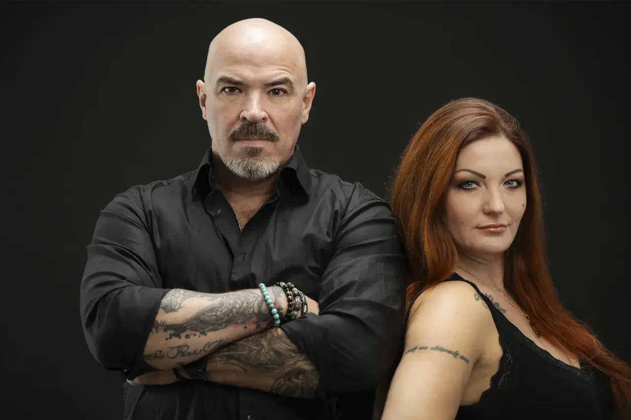 Caroline Grimwalker och en man med tatueringar och skägg står mot en svart bakgrund.