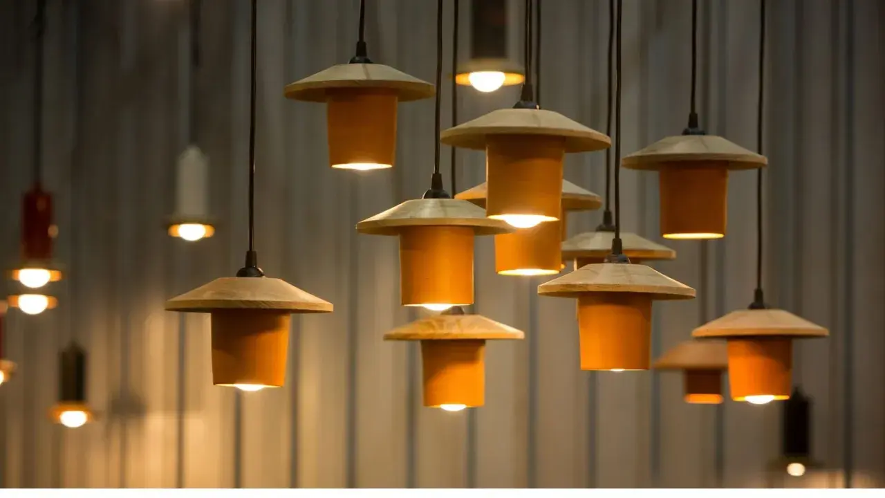 Un grupo de lámparas colgantes de diseño moderno, con pantallas de madera y cilindros naranjas, iluminan el espacio.