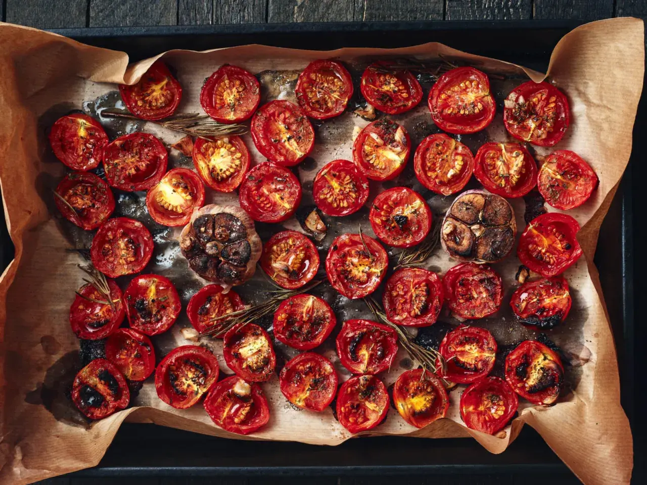 Pomodorini al forno, caramellati e profumati al rosmarino, con teste d'aglio arrostite.