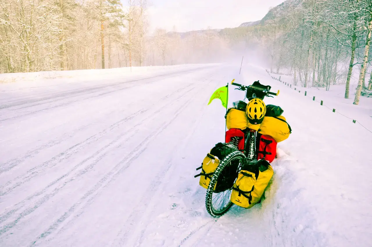 A fully loaded bicycle sits on a snowy road, a testament to adventure. The rider's concern about the brake fluid freezing point is evident in this winter scene.