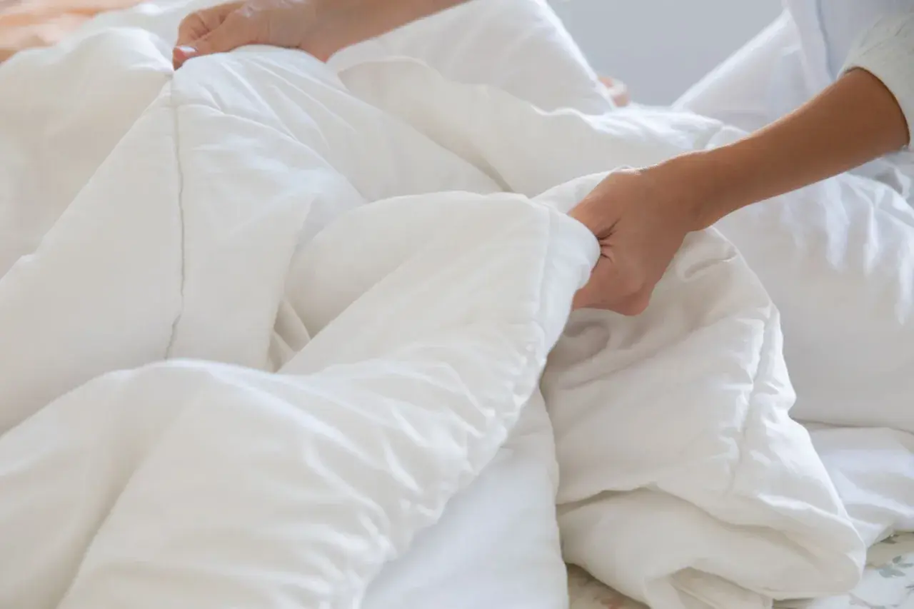 Hands smoothing a white duvet, a step in how to wash bedding for a fresh, clean sleep.