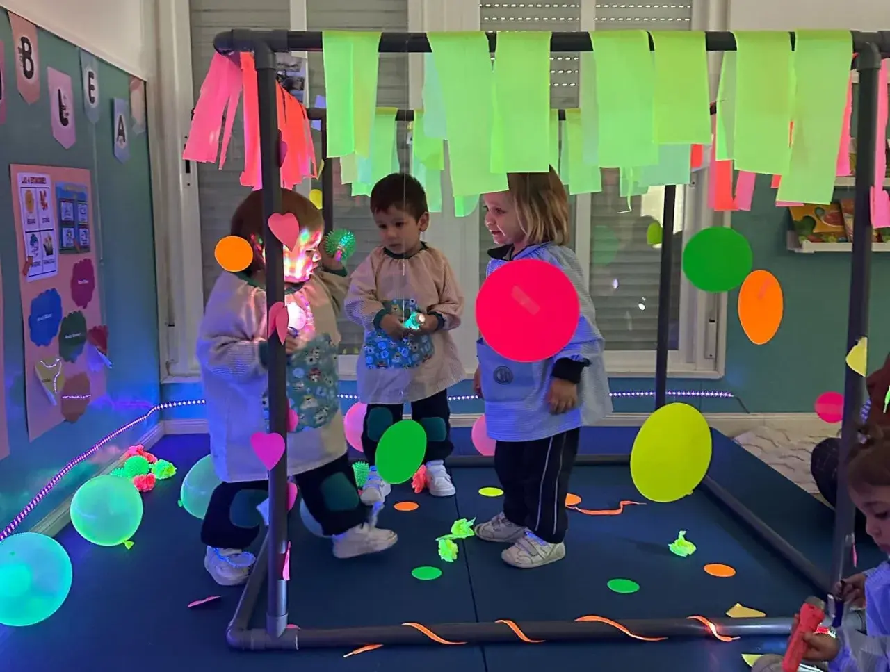 Niños explorando un aula multisensorial infantil con luces de neón, globos y elementos interactivos.