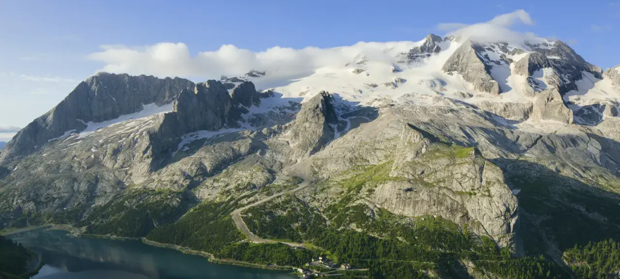 Majestätischer Marmolada Gletscher, umgeben von felsigen Gipfeln und grünen Hängen, mit einem See im Vordergrund.