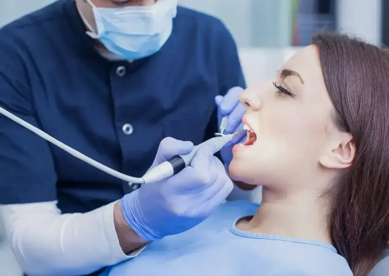 Dentysta w masce i rękawiczkach wykonuje zabieg. Zastanawiasz się, ile kosztuje znieczulenie u dentysty?