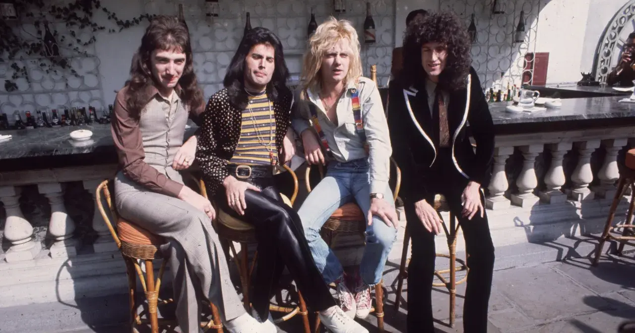 Freddie Mercury i zespół Queen siedzą przy barze w słoneczny dzień.