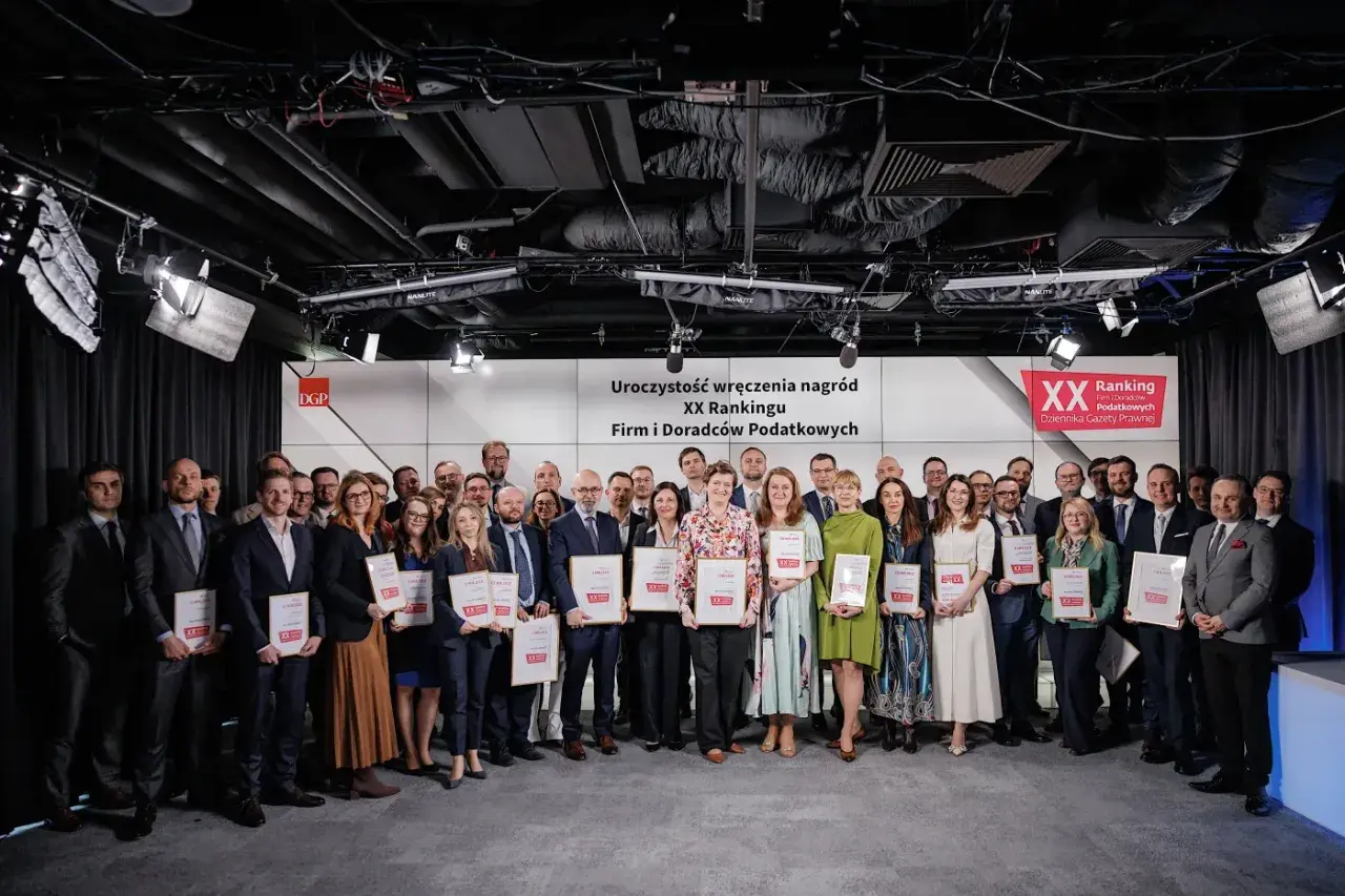 Grupa osób w garniturach i sukienkach pozuje do zdjęcia z nagrodami.