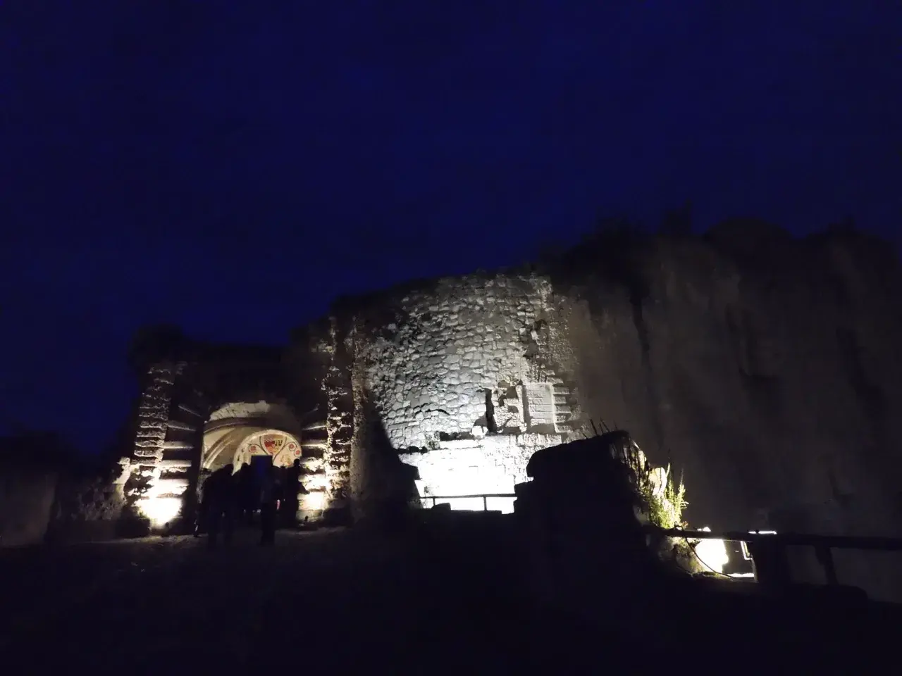 Nuit tombante sur un château abandonné dans la Somme. Des lumières éclairent l'entrée voûtée et les vieilles pierres.
