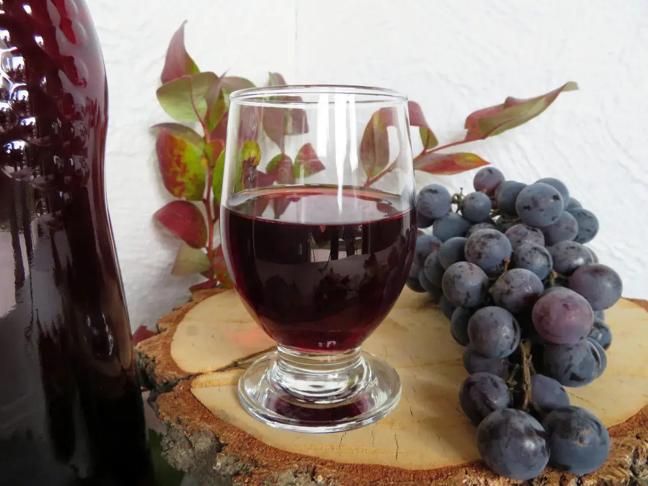 Ciemnoczerwone wino w kieliszku, obok kiść winogron i butla. Idealne do domowego wina w 5 litrowej butli.