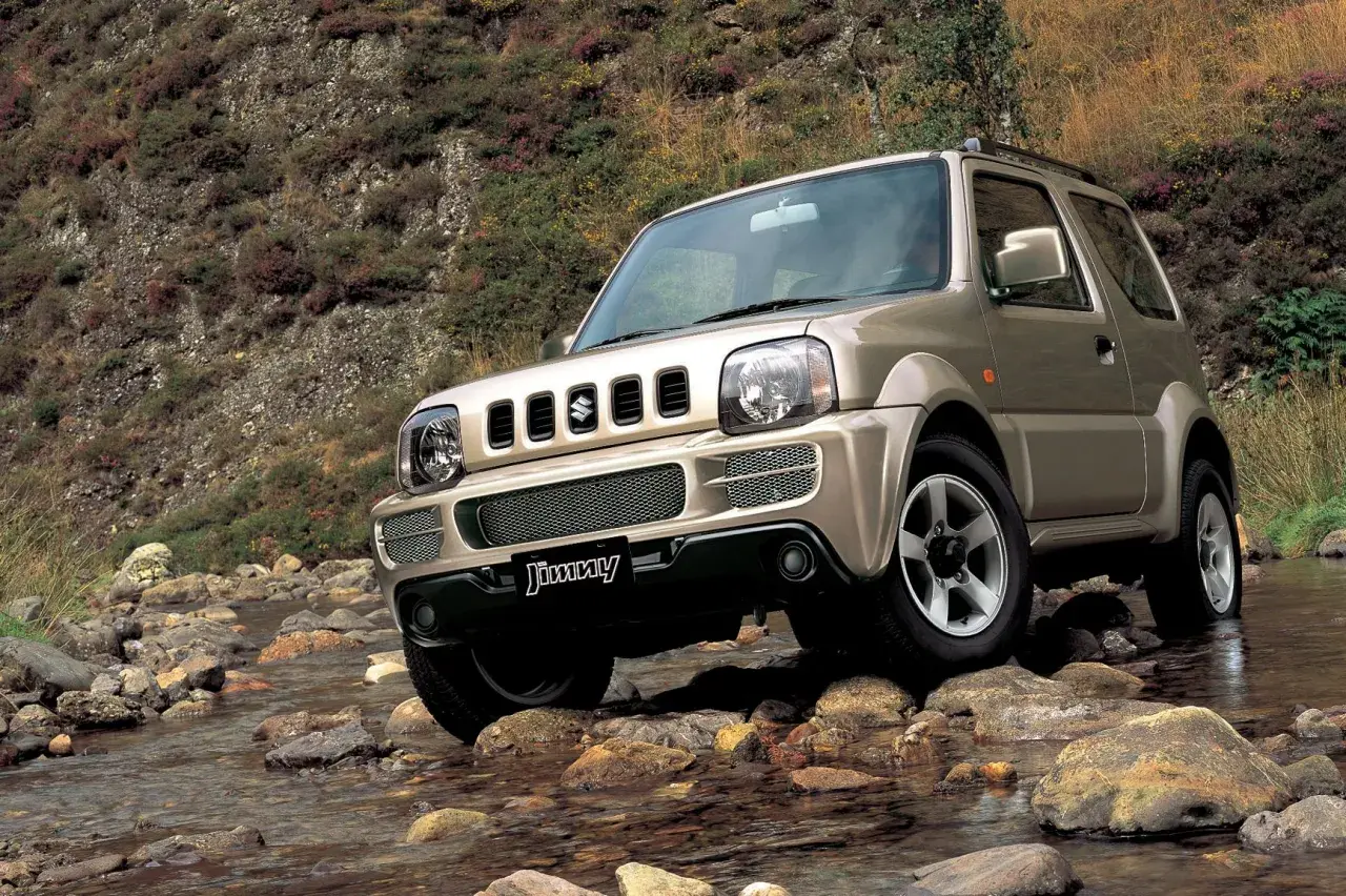 Złoty Suzuki Jimny (1998) pokonuje kamienisty strumień, gotowy na każdą przygodę.