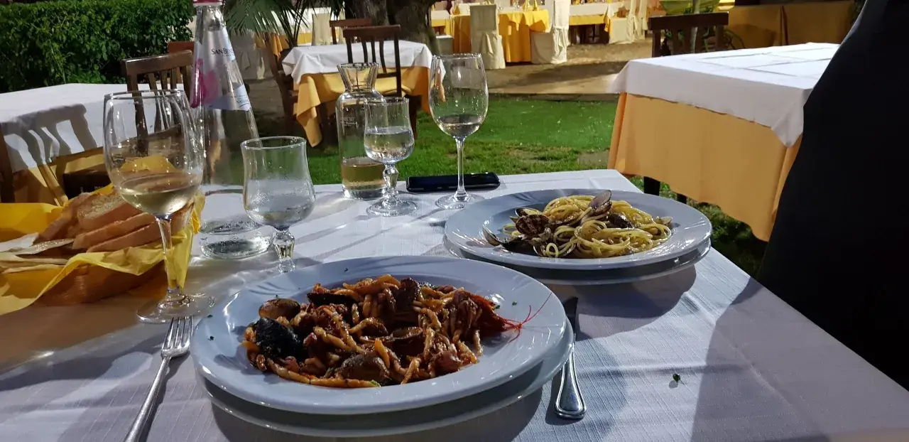 Dwa talerze z makaronem i owocami morza, kieliszki z winem i woda na stole w restauracji pod gołym niebem.