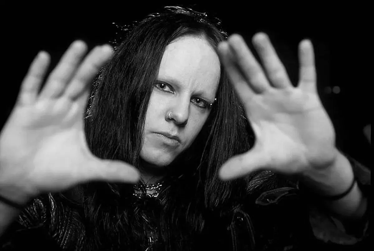 Joey Jordison, perkusista zespołu Slipknot, z rękami przed twarzą, w czerni i bieli.