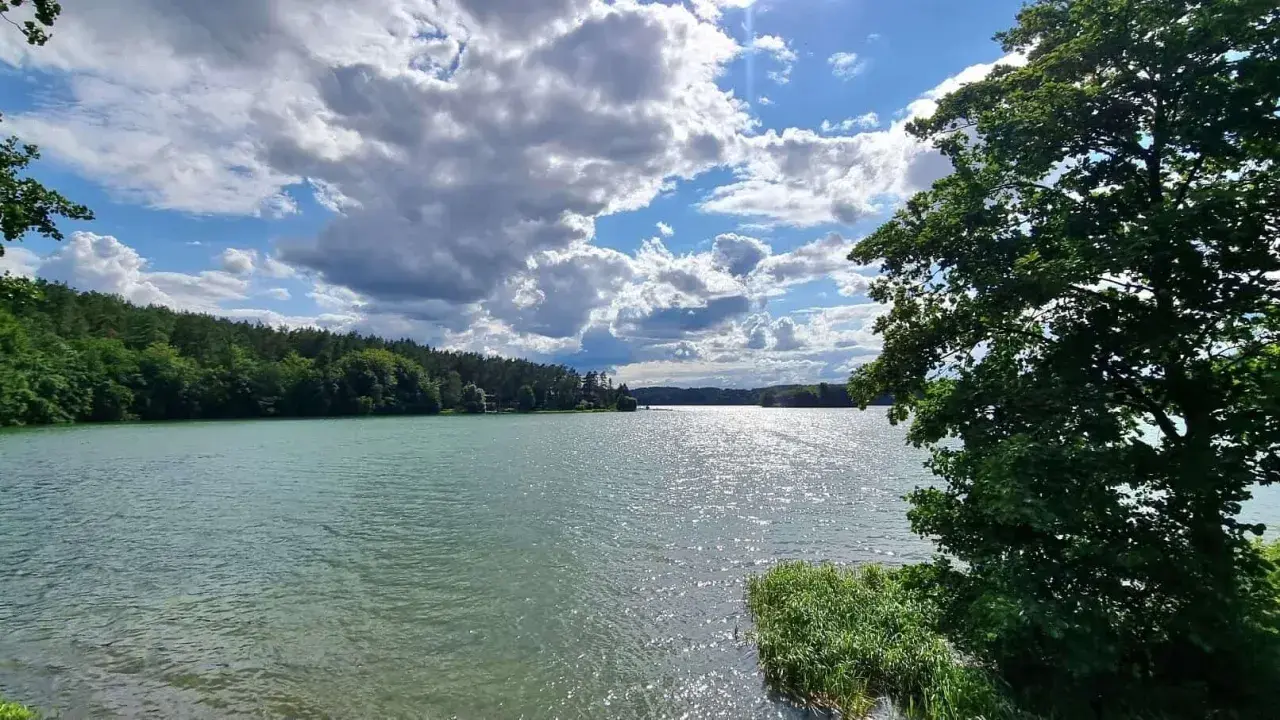 Spokojne jezioro na Kaszubach, otoczone lasem, z chmurami na niebie. To jak brama kaszubska do natury.