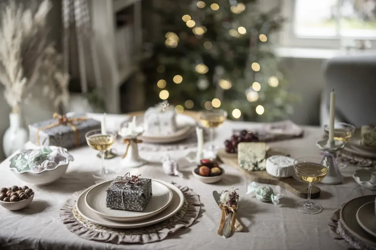 Elegant Christmas tablescape ideas: a festive table set with gifts, cheese, grapes, and champagne, with a blurred Christmas tree in the background.