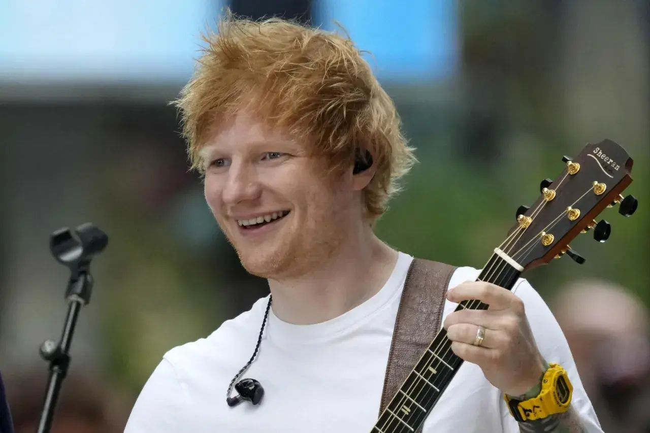 Ed Sheeran uśmiecha się, grając na gitarze podczas koncertu w Polsce.