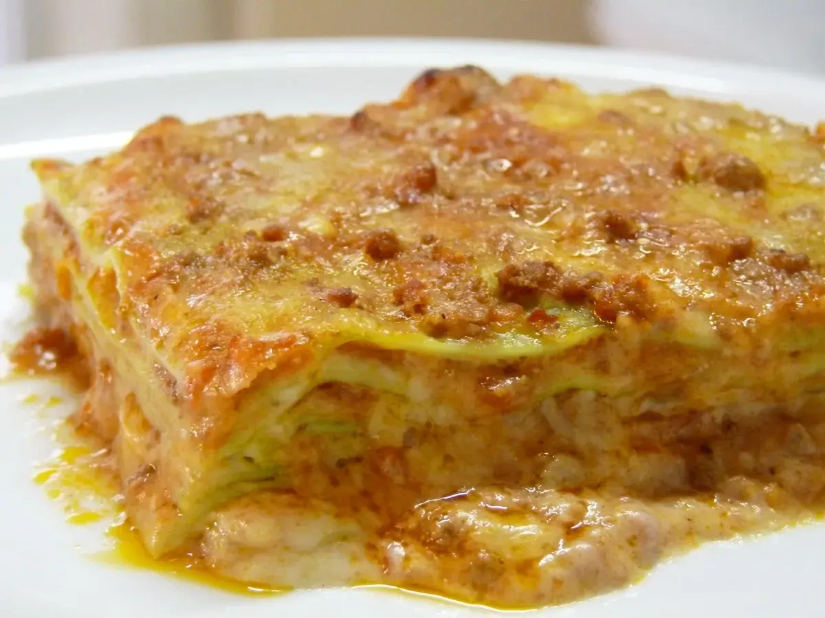Une part de lasagne généreuse, aux couches de pâtes, sauce bolognaise et béchamel, évoquant la richesse de la lasagne origine.