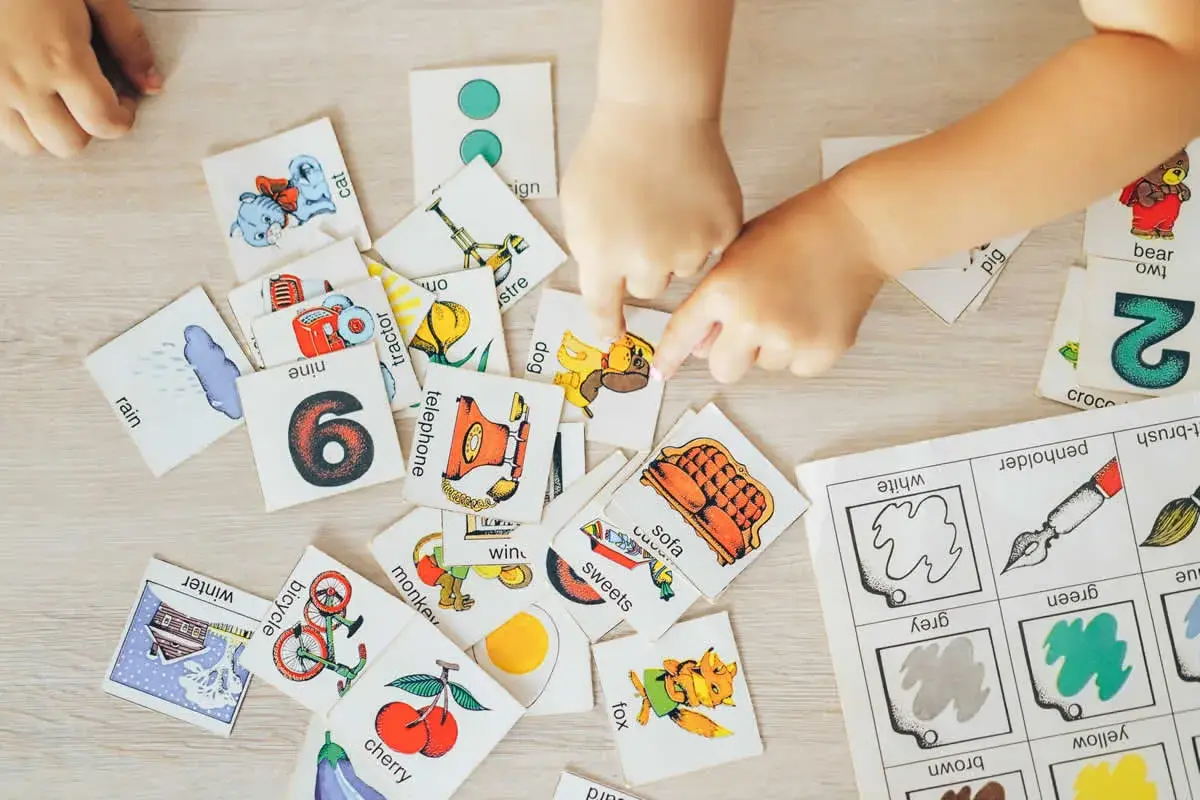 Manos de niños jugando con tarjetas de aprendizaje, practicando ejercicios de memoria con imágenes de animales, números y objetos.