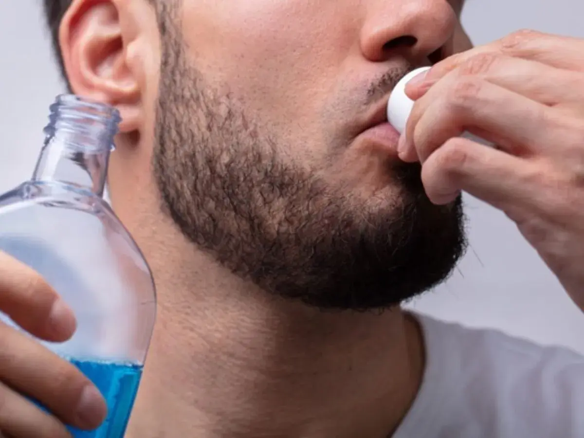 Uomo usa collutorio per parodontite, tenendo una bottiglia di liquido blu.