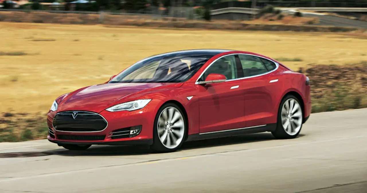 Czerwony Tesla Model S pędzi po drodze, otoczony suchymi, trawiastymi krajobrazami.