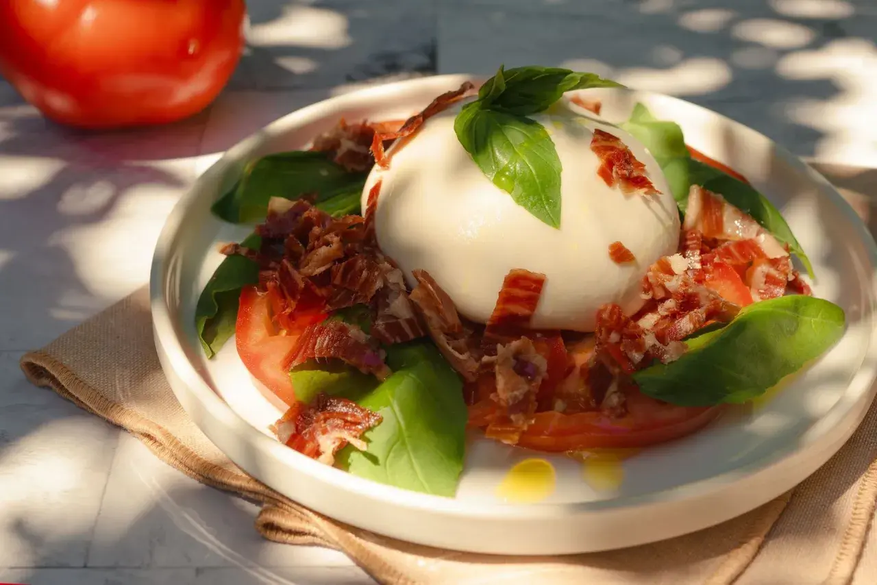 Deliciosa ensalada de burrata con tomates, albahaca fresca y crujiente jamón serrano.