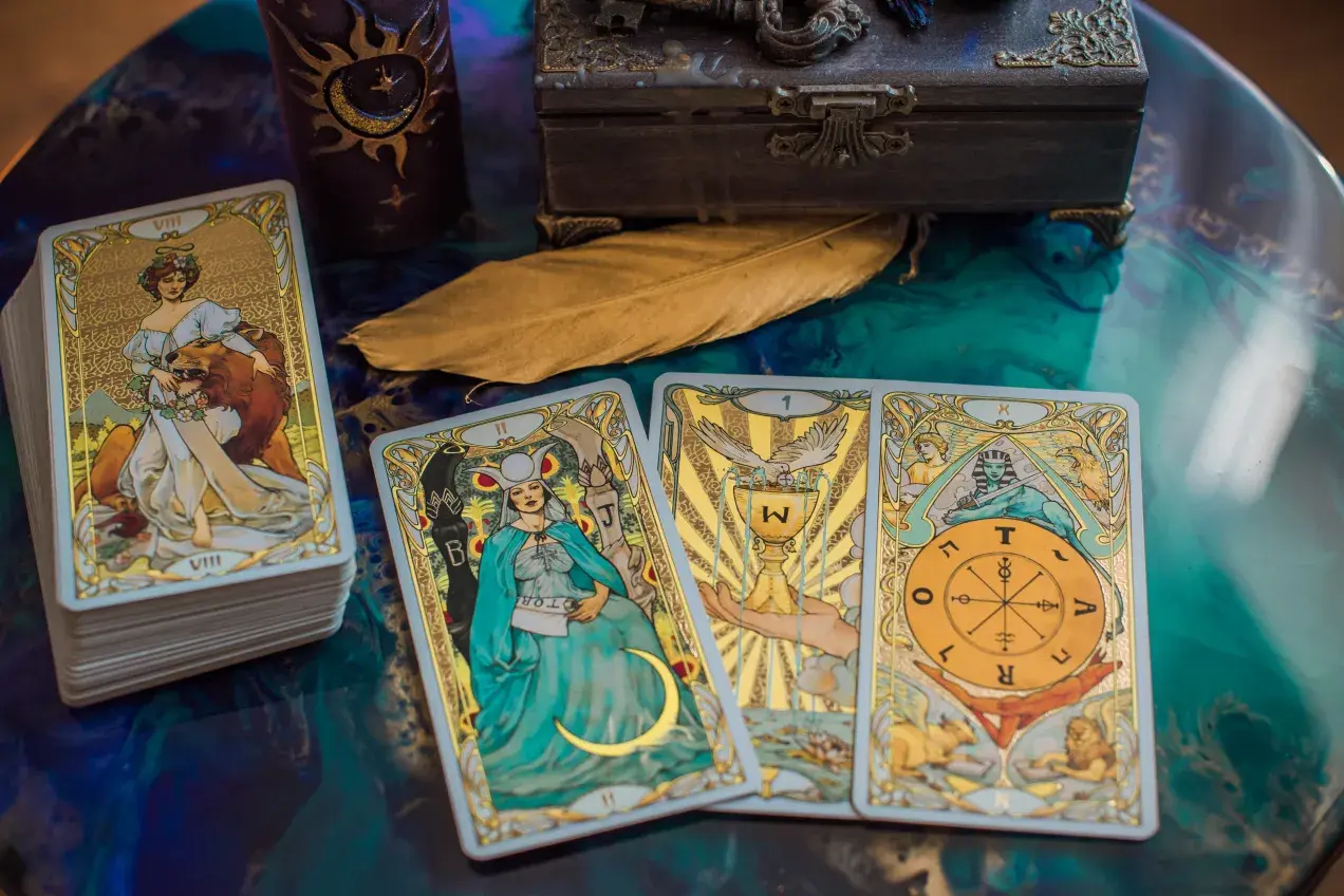 Tarot byk miesięczny: talia kart z wizerunkami postaci i symboli, w tym karta z bykiem, świeca, skrzynia i pióro.