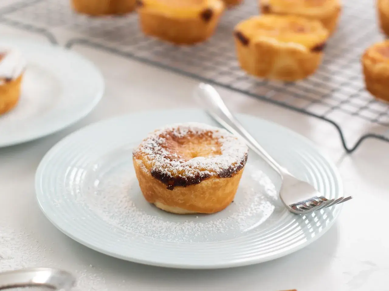 Un delizioso pastel de nata, cosparso di zucchero a velo, su un piatto azzurro con una forchetta.