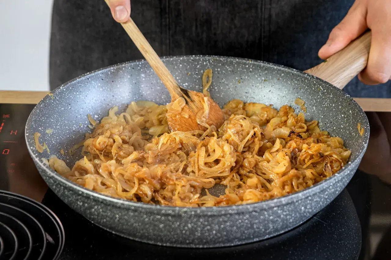 Omas Zwiebelrostbraten wird in der Pfanne zubereitet. Zwiebeln werden goldbraun gebraten, ein köstlicher Duft liegt in der Luft.