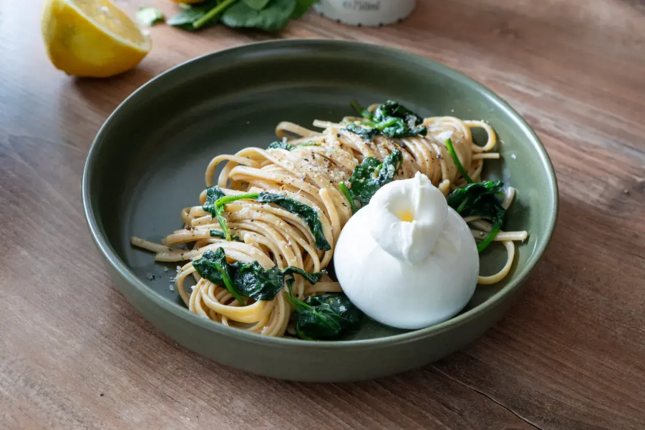 Zitronen Pasta mit Spinat und Burrata auf einem grünen Teller, daneben eine Zitronenhälfte.