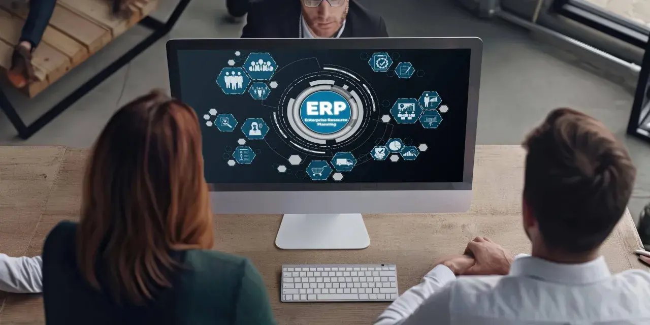 Zespół analizuje diagram ERP na ekranie komputera. Ikony symbolizują różne moduły systemu, od zarządzania zasobami ludzkimi po logistykę.