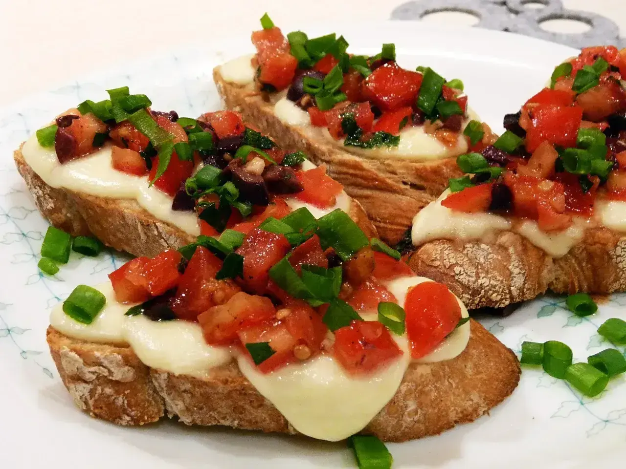 Bruschetta z pomidorami i mozzarellą: chrupiące grzanki z roztopionym serem, świeżymi pomidorami, oliwkami i szczypiorkiem. Idealny przepis na szybką przekąskę.