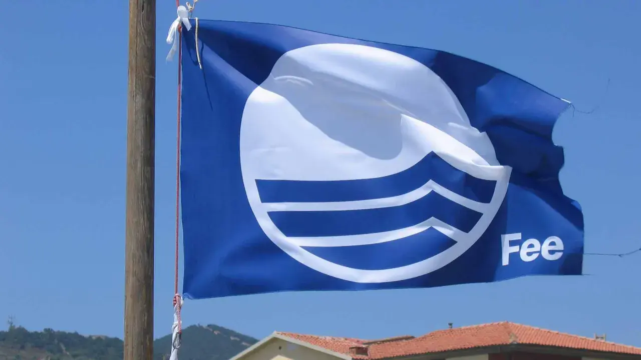 Bandiera blu con logo FEE sventola su un cielo azzurro, simbolo di qualità ambientale.