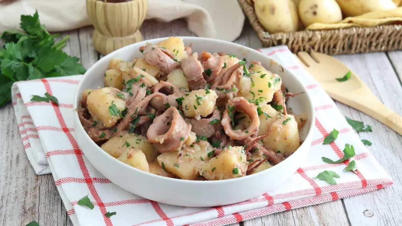 Un saporito piatto di totani e patate, condito con prezzemolo fresco, servito in una ciotola bianca su un tovagliolo a quadri rossi.