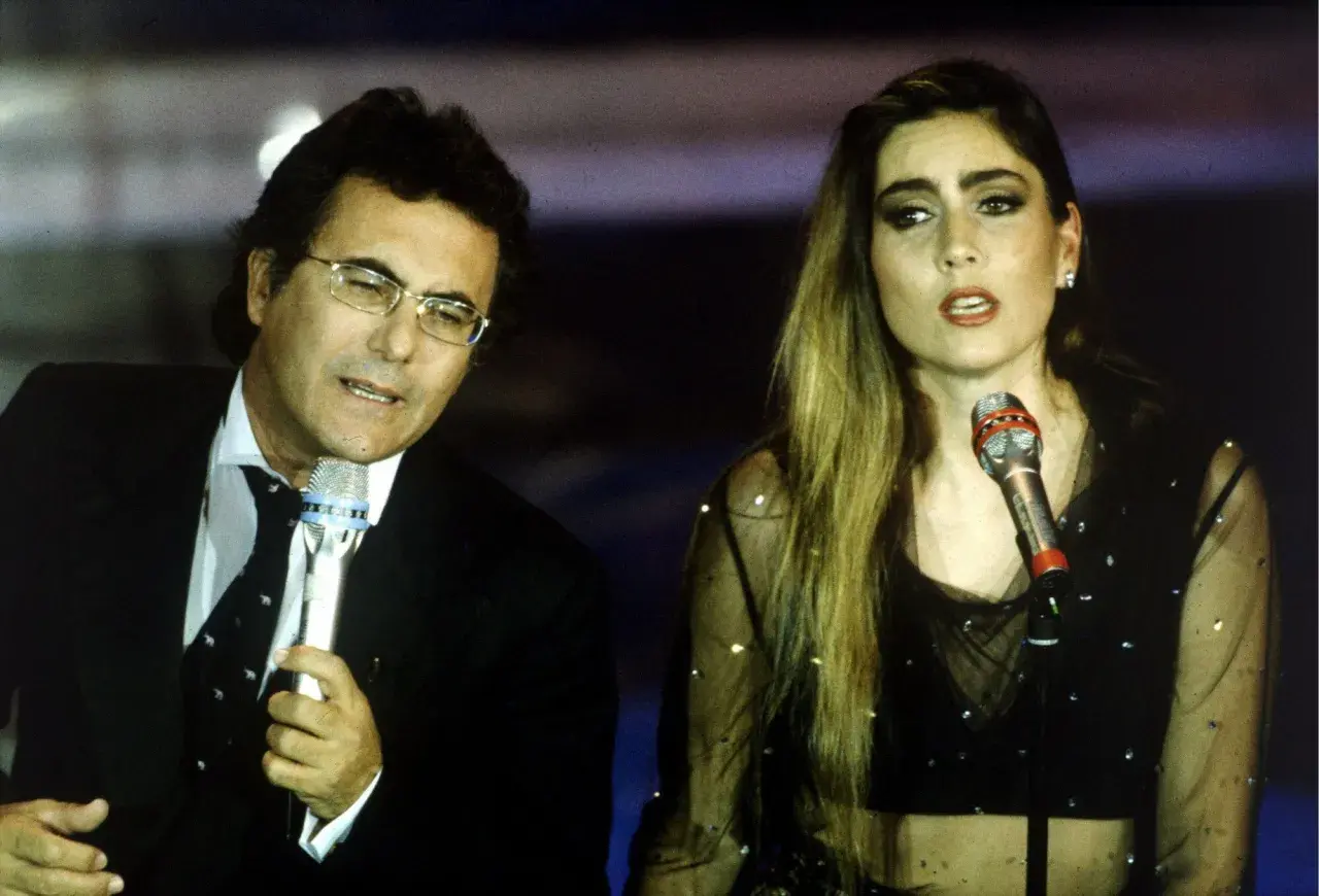 Al Bano i jego nowa partnerka na scenie, w blasku świateł, śpiewają do mikrofonów.