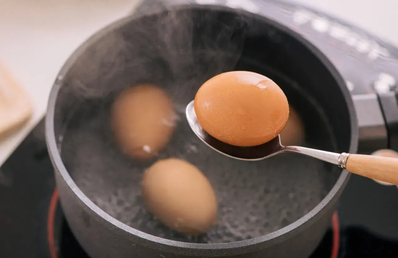 Une cuillère sort un œuf à la coque de l'eau bouillante. Trois autres œufs sont dans la casserole.